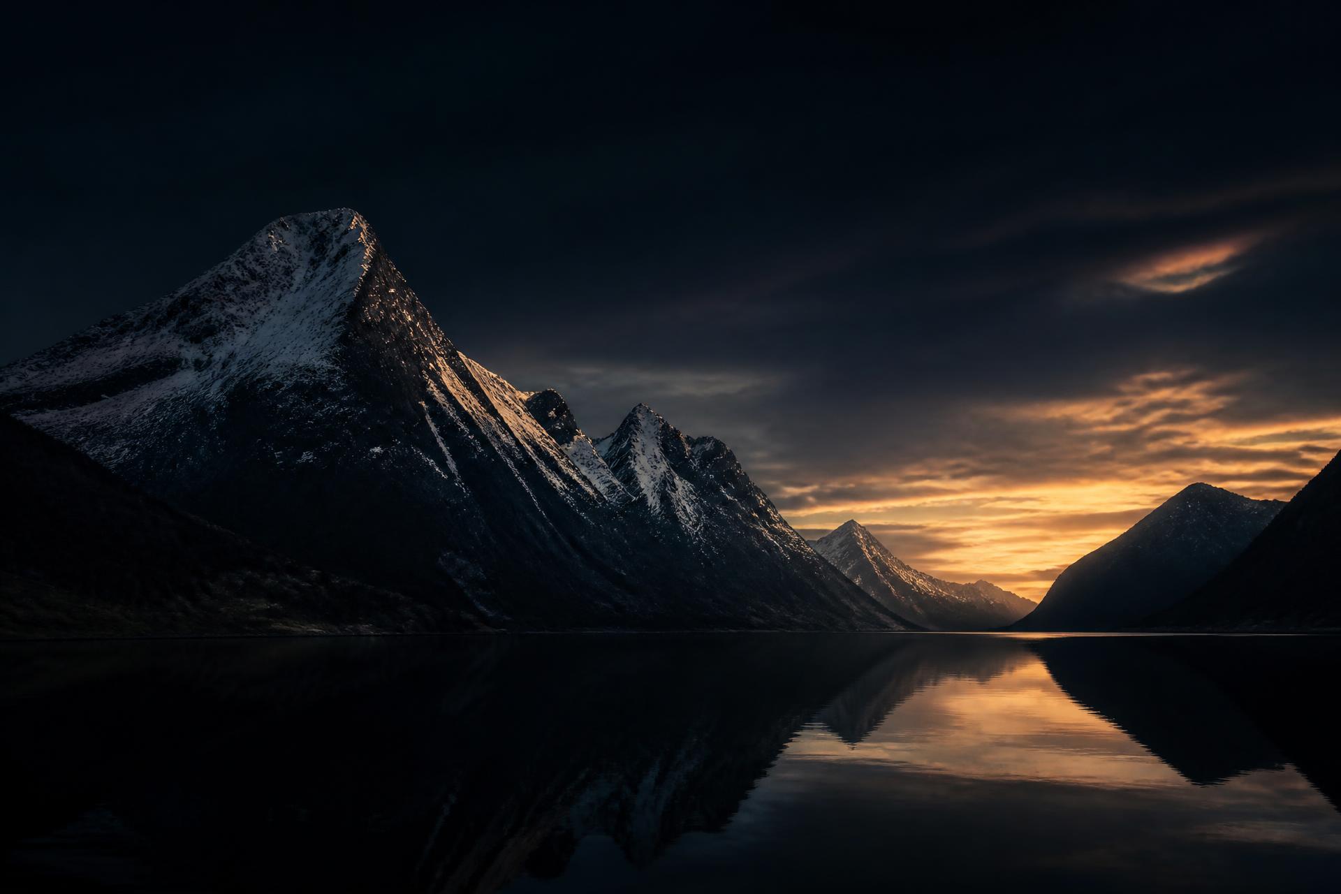 Snöklädda fjällmassiv speglas i en stilla fjord i gryningsljus